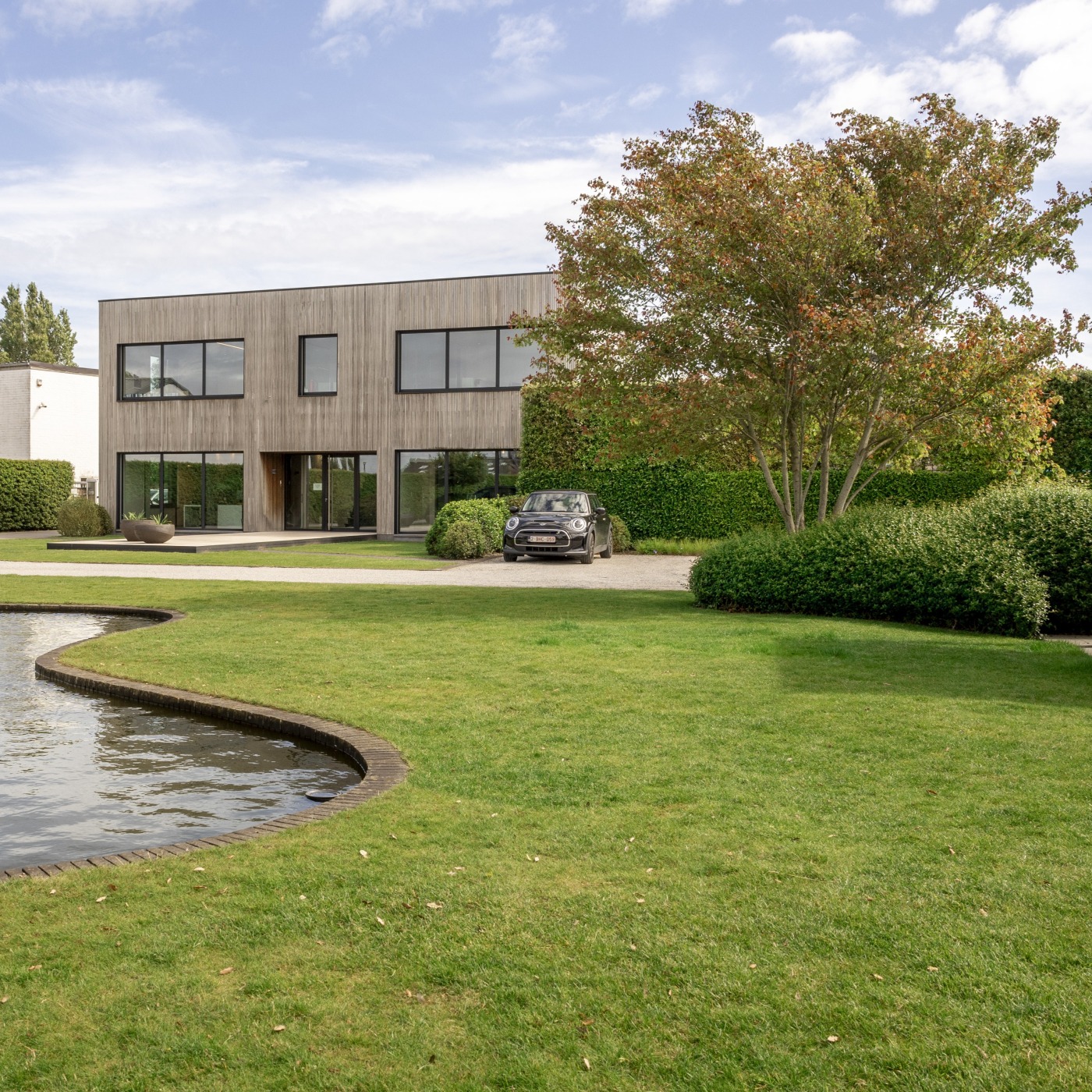 De showtuin van Castelein Outdoor, met een vijver en strak gemaaid gazon bij een moderne woning.