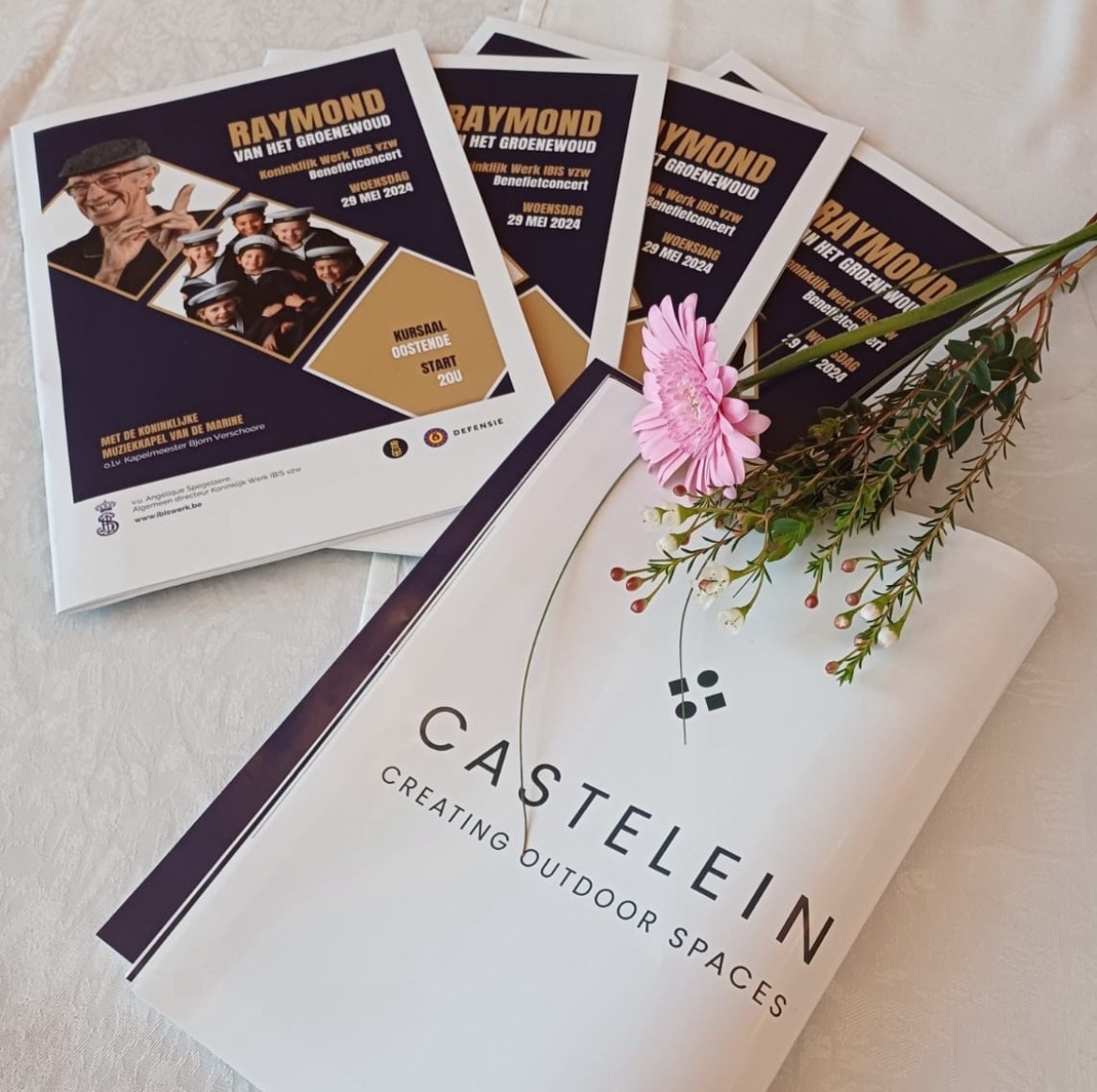 Programma's van het benefietconcert, gesponsord door Castelein Outdoor, met een bloemenarrangement op de voorgrond