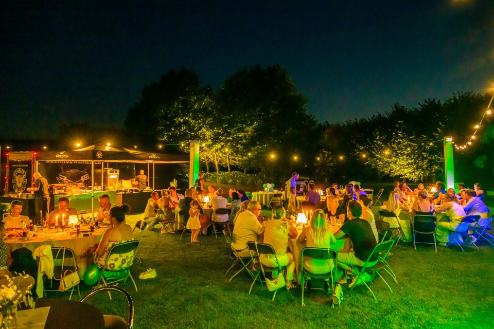 Sfeerbeeld van de avond, met mensen die genieten van hun maaltijd onder sfeerverlichting.
