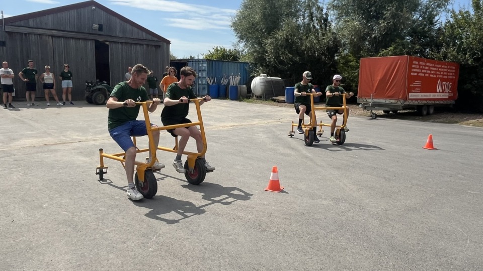 Twee ploegen racen op driewielers terwijl collega's toekijken tijdens een teambuildingactiviteit.