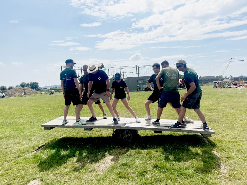 Medewerkers van Castelein Outdoor balanceren samen op een plank tijdens een teambuildingactiviteit.
