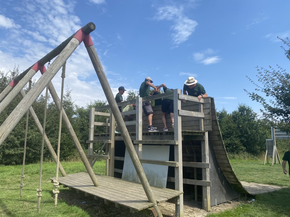 Collega’s klimmen over een houten obstakel tijdens een uitdagende teambuildingactiviteit.