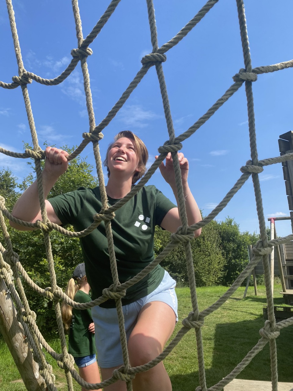 Een lachende deelnemer klimt door een touwnet tijdens de teambuilding bij Castelein Outdoor.